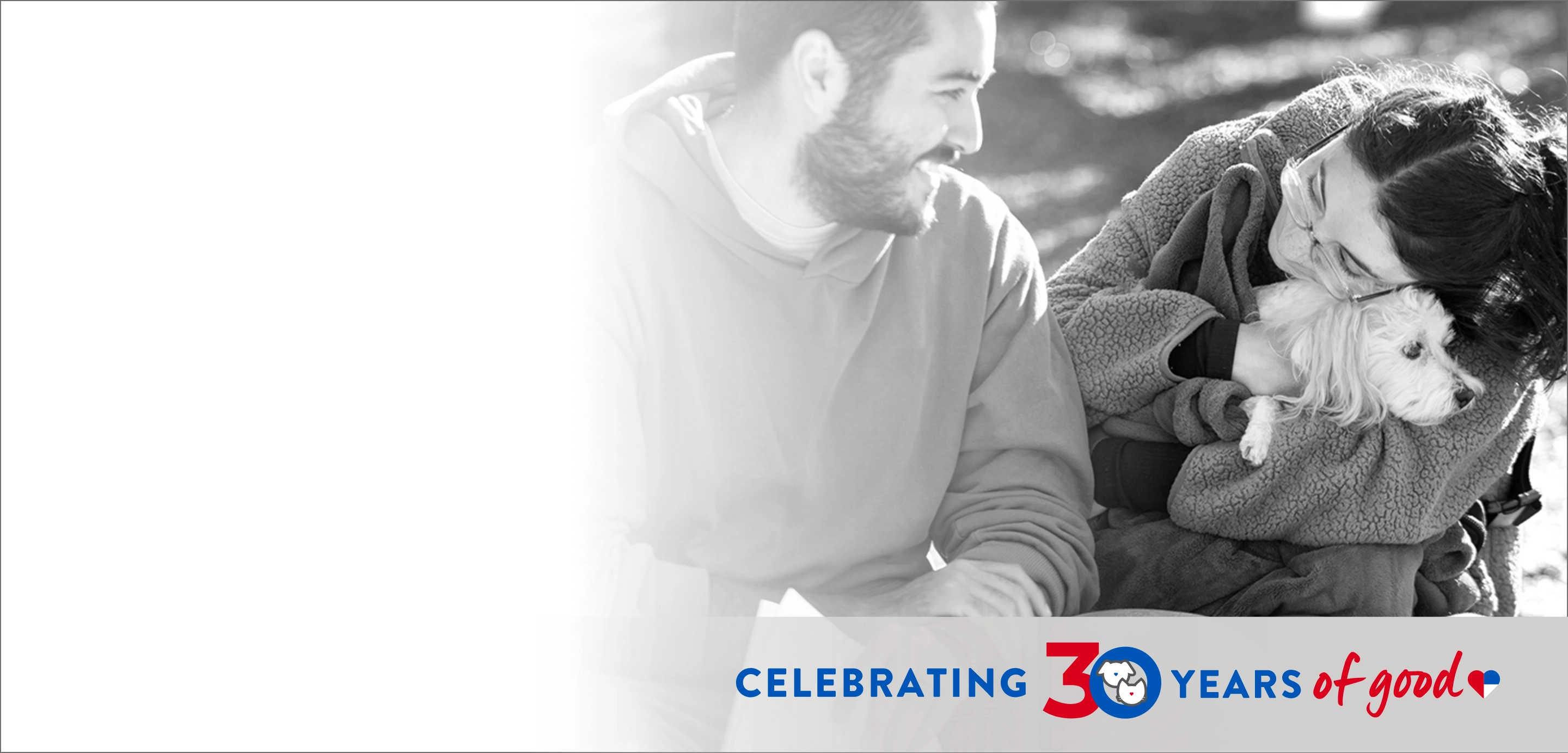 Man looks at a woman hugging a small dog in her arms, text that reads "Celebrating 30 years of Good"